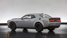 the rear end of a gray sports car on a black floor in front of a white wall