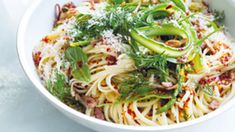 a white bowl filled with pasta and vegetables on top of a table next to a fork