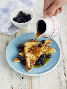 someone pouring syrup on some french toast with blueberries