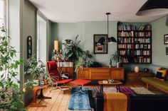 a living room filled with furniture and bookshelves next to a window covered in plants