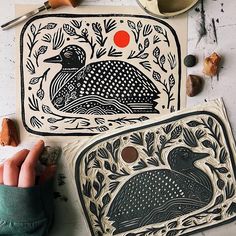 two handmade pottery pieces on a table with various tools and supplies around them, including a bird design