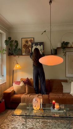 a woman standing on top of a couch in a living room next to a window