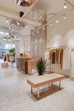 the inside of a clothing store with clothes hanging on racks and plants in vases