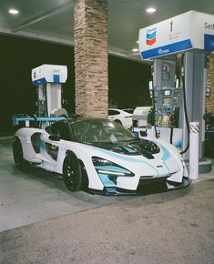 a white and blue sports car parked in front of a gas pump at a station