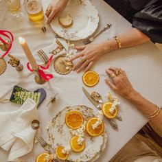 people are sitting at a table with orange slices and silverware on it, eating