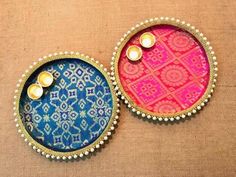 two small trays with buttons and beads on top of a brown cloth covered surface