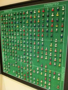 a soccer field is covered with many small figurines on display in front of a black framed poster