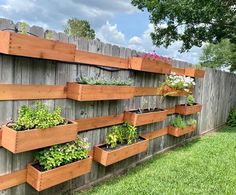 several wooden planters are lined up against a fence with flowers growing in the bottom row