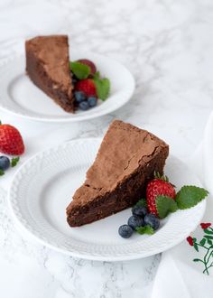 two white plates topped with slices of chocolate cake and strawberries next to each other