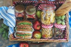 a picnic basket filled with sandwiches, fruit and other foods on a blanket next to some bread