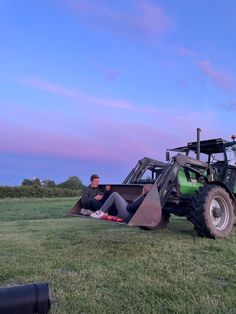 a man sitting in the back of a tractor on top of a lush green field