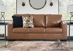 a brown leather couch sitting in front of a mirror on a wall next to two lamps