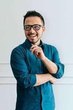 a man with glasses is smiling and looking at the camera while standing in front of a white wall