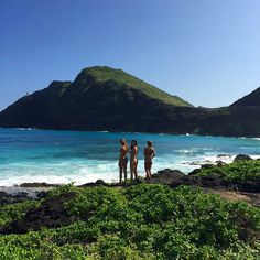 three people standing on the beach looking out at the water and mountains in the distance