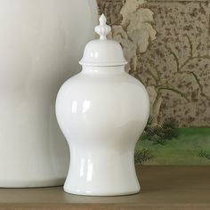 a white vase sitting on top of a table next to a wallpapered background