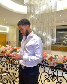 a man in a white shirt and black pants standing next to a table with flowers