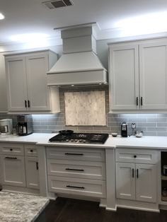 a kitchen with white cabinets and marble counter tops, along with stainless steel hoods