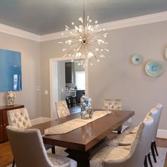 a dining room table with white chairs and a chandelier hanging from the ceiling