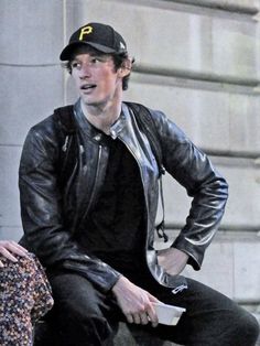 a man sitting on top of a stone wall next to a woman wearing a hat