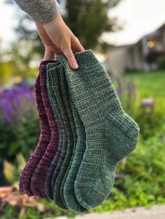 a person holding three pairs of socks in their hand, one is green and the other is purple