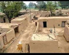 an aerial view of a village with adobe buildings and people in the distance, surrounded by trees