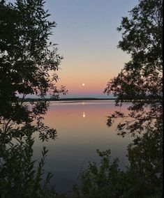 the sun is setting over water with trees around it