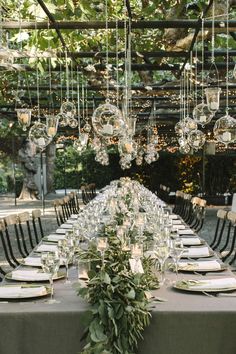 a long table set up with place settings and hanging glass globes for the centerpieces