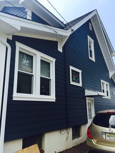 a car is parked in front of a house with blue siding and white trim on the windows