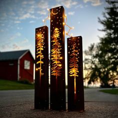 three tall metal sculptures with lights on them in front of a red barn and trees