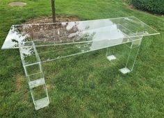 a clear glass table sitting on top of a lush green grass covered field next to a tree