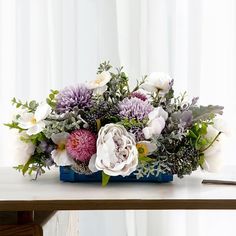 a bouquet of flowers sitting on top of a wooden table next to a white curtain