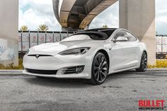 a white tesla model s is parked under a bridge