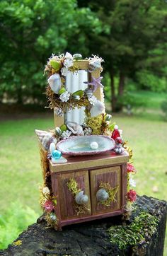 an old dresser is decorated with flowers and seashells in the grass by some trees