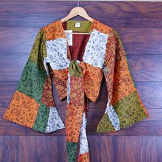 Add a dash of bohemian charm to your wardrobe with this colorful paisley print bell sleeve patchwork top. Perfect for festival lovers and free-spirited souls alike. Design & Print: Paisley Print: Features a whimsical mix of paisley prints in earthy tones. Colorful Patchwork: Crafted from a vibrant combination of warm colors including oranges, greens, and browns. Bell Sleeves & Crop Length: Bell Sleeves: Wide, flowing sleeves add a dramatic and stylish flair. Crop Length: Finished with a flattering tie-front closure at the waist. Material & Fit: Material: Made from lightweight and breathable cotton for comfort. Fit: Relaxed fit makes it ideal for layering over a tank top or bikini. Boho Style: Perfect for music festivals, beach outings, or casual everyday wear. Embodies the free-spirited hi Multicolor Floral Patchwork Long Sleeve Top, Multicolor Long Sleeve Top With Floral Patchwork, Green Boho Print Long Sleeve Top, Green Long Sleeve Top With Boho Print, Cotton Patchwork Long Sleeve Blouse, Green Long Sleeve Boho Print Top, Hippie Patterned Tops For Fall, Patterned Long Sleeve Blouse For Festivals, Bohemian Cotton Tops For Fall