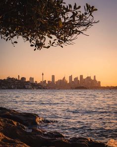 the sun is setting over the city skyline as it reflects in the water and rocks