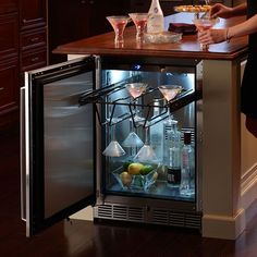 a woman standing in front of an open refrigerator with drinks on the door and wine glasses