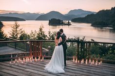 a bride and groom standing on a deck with candles in front of them at sunset