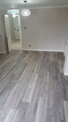 an empty room with hard wood flooring and white painted walls in the background is a doorway leading to another room