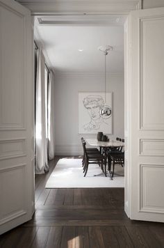 an open door leading to a dining room with white walls and wood floors, along with a painting on the wall