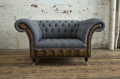 an old fashioned grey couch sitting on top of a wooden floor next to a white brick wall