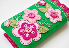 a green case with pink flowers and buttons on the front is sitting on a white surface