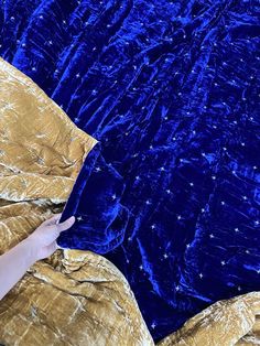 a person laying on a bed covered in blue and gold velvets with their hand under the covers