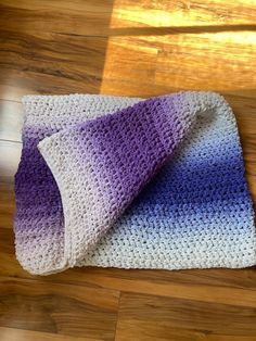 a crocheted blanket laying on top of a wooden floor next to a pillow