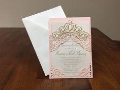 a pink and gold wedding card on top of a wooden table with a white envelope