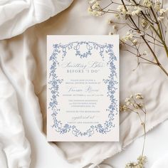 a white and blue wedding card on top of a bed next to some dried flowers