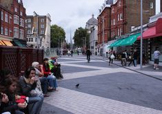 people are sitting on benches in the middle of an empty street with shops and pedestrians