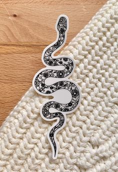 the snake sticker is laying on top of a white knitted blanket with wood flooring in the background