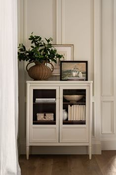 a white cabinet with some books and a potted plant