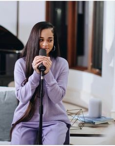 a woman with long hair sitting on a couch and holding a microphone in her hands