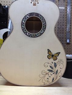 a white guitar with a butterfly painted on it's back and sides sitting on a table